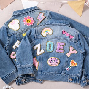 May include: Two light blue denim jackets with colourful patches. One jacket has a flower, cloud, and lightning bolt patch. The other jacket has a rainbow, hearts, and the name "ZOEY" spelled out with patches, plus a donut and a heart-shaped lollipop.