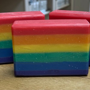 May include: Three rectangular bars of soap with a rainbow color scheme. The soap bars are arranged with the colors of the rainbow, from red at the top to purple at the bottom. The soap is a solid color and has a smooth texture.