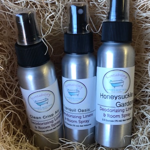 Pode incluir: Tr&ecirc;s frascos de spray prateados com tampas pretas e r&oacute;tulos brancos, aninhados em palha. Os r&oacute;tulos dizem "Clean Crisp Air", "Tranquil Oasis" e "Honeysuckle Garden" spray desodorizante para roupa de cama e ambiente. Cada frasco cont&eacute;m 75 ml.