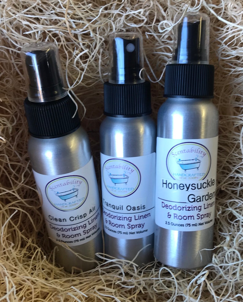 Pode incluir: Tr&ecirc;s frascos de spray prateados com tampas pretas e r&oacute;tulos brancos, aninhados em palha. Os r&oacute;tulos dizem "Clean Crisp Air", "Tranquil Oasis" e "Honeysuckle Garden" spray desodorizante para roupa de cama e ambiente. Cada frasco cont&eacute;m 75 ml.