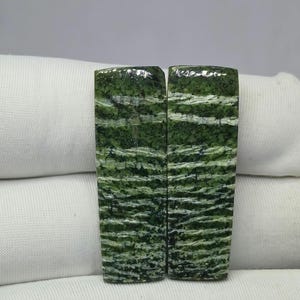 May include: Two rectangular polished stone slabs featuring a deep forest green base color with intricate, horizontal white and light green veining patterns. The surfaces are smooth and glossy, displaying a natural mottled texture throughout the stone.