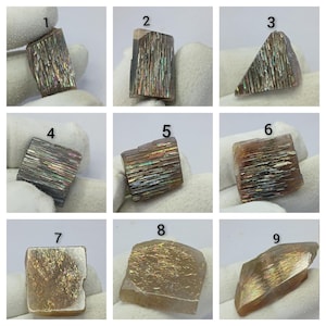 May include: A collection of nine individual sunstone mineral specimens, each labelled with a number from one to nine. These stones exhibit varying shapes and sizes, featuring internal metallic inclusions that create iridescent, rainbow-like light reflections.