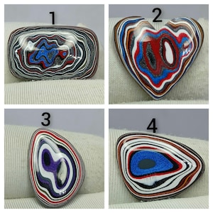 Puede incluir: Cuatro cabujones pulidos con patrones de múltiples colores en capas. El número 1 es rectangular, el 2 tiene forma de corazón, el 3 tiene forma de lágrima con morado y el 4 es un triángulo redondeado con un centro azul. Cada pieza muestra líneas concéntricas onduladas.