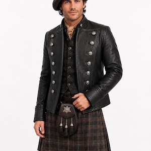 Könnte beinhalten: Eine dunkelgraue Wollbaskenmütze, eine schwarze Lederjacke im Militärstil mit silbernen Knöpfen, eine dunkle strukturierte Weste, ein beiges Halstuch und ein braun-schwarz karierter Kilt mit einer Ledertasche, die ein silbernes Emblem trägt.