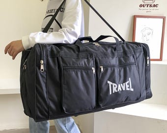 May include: A black travel duffel bag with multiple zippered compartments and a shoulder strap. The word "TRAVEL" is printed in white on the front. The bag is being carried by a person.