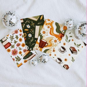 Puede incluir: Una colección de estampados cuadrados decorativos con diseños florales, de libros y de café. Los estampados muestran una variedad de colores, incluyendo naranja, verde y marrón, con patrones de margaritas y hojas. Bolas de discoteca plateadas están dispersas alrededor de los estampados.