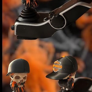 May include: Black and orange skull-themed joystick with a black baseball cap. The skull has an orange and black beard. The joystick is black with silver accents and a Harley-Davidson logo on the cap.