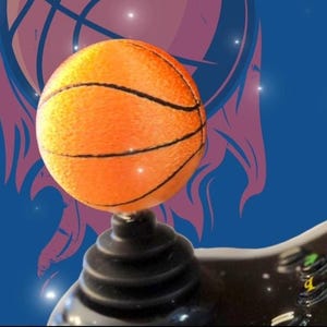 May include: An orange basketball with black lines, set against a blue background with a basketball graphic. The basketball is balanced on a black, tiered base, creating a dynamic sports-themed image.