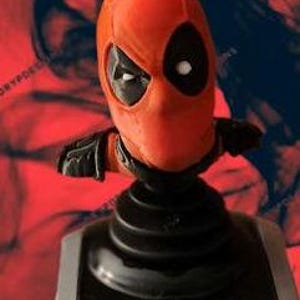 May include: A red and black Deadpool bobblehead. The head is red with black eye cutouts and a white dot for the eye. The bobblehead is mounted on a black base with a silver-colored control panel.