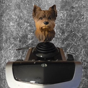 May include: A brown and tan Yorkshire Terrier dog head sculpture mounted on a black joystick controller. The dog figure features detailed fur texture, pointed ears, and a black nose, positioned atop a black circular base with a silver-trimmed console.