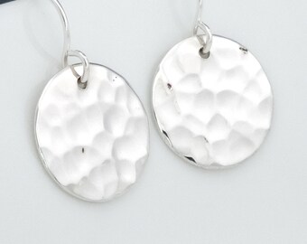May include: A pair of silver hammered disc earrings with a smooth, rounded finish. The earrings are suspended from a simple silver hook.
