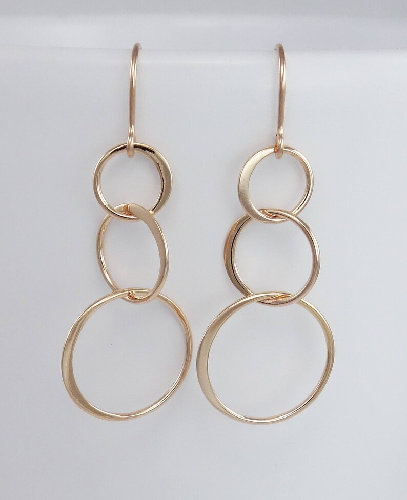 Peut inclure: Boucles d'oreilles en or avec trois cercles entrelac&eacute;s. Les cercles sont de tailles diff&eacute;rentes et sont reli&eacute;s &agrave; un crochet.