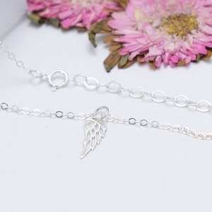 May include: A delicate silver chain necklace with a small, detailed silver angel wing charm. The chain is made of small, round links.