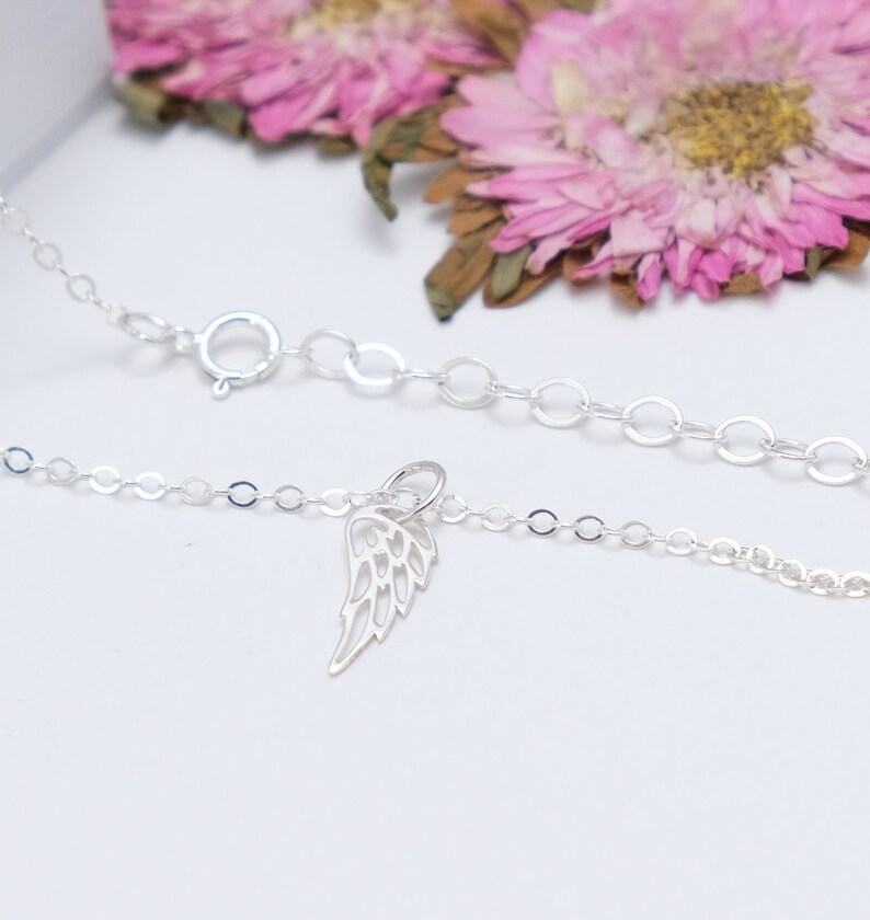 May include: A delicate silver chain necklace with a small, detailed silver angel wing charm. The chain is made of small, round links.