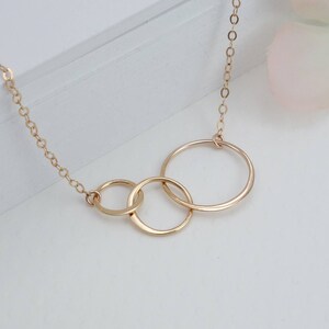 Peut inclure: Un collier en or avec trois cercles entrelac&eacute;s. Les cercles sont de tailles diff&eacute;rentes et sont reli&eacute;s &agrave; une cha&icirc;ne d&eacute;licate.