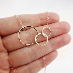 Peut inclure: Un collier en or avec trois cercles entrelac&eacute;s. Les cercles sont de tailles diff&eacute;rentes et sont reli&eacute;s les uns aux autres. Le collier est sur une main.