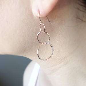 Peut inclure: Boucles d'oreilles pendantes en or rose avec trois cercles interconnect&eacute;s.