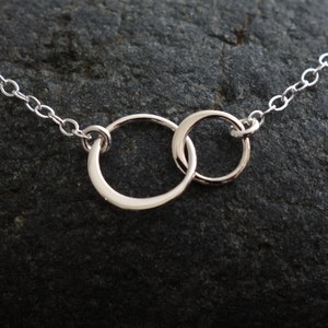 May include: A silver necklace with a delicate chain and two interlocking circles pendant.