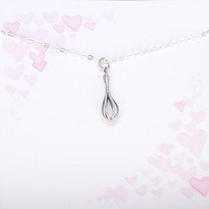 Puede incluir: Un collar de plata con un peque&ntilde;o dije de batidor. El collar est&aacute; sobre un fondo blanco con corazones rosas de acuarela.