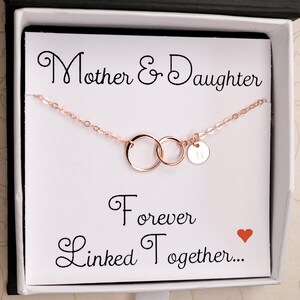 Pode incluir: Um colar de ouro rosa com dois c&iacute;rculos entrela&ccedil;ados e um pequeno pingente com a letra "N". O colar est&aacute; em uma caixa branca com um cart&atilde;o que diz "M&atilde;e e Filha Para Sempre Unidas..." com um cora&ccedil;&atilde;o vermelho.