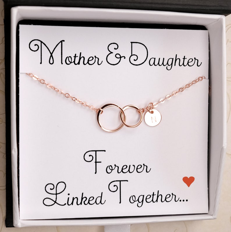 Pode incluir: Um colar de ouro rosa com dois c&iacute;rculos entrela&ccedil;ados e um pequeno pingente com a letra "N". O colar est&aacute; em uma caixa branca com um cart&atilde;o que diz "M&atilde;e e Filha Para Sempre Unidas..." com um cora&ccedil;&atilde;o vermelho.