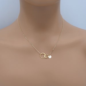 Pode incluir: Colar de ouro com dois c&iacute;rculos entrela&ccedil;ados e um pequeno pingente redondo com a letra 'A' gravada.
