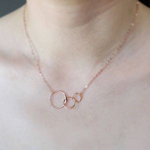 Peut inclure: Un collier en or rose avec trois cercles entrelac&eacute;s. Les cercles sont de tailles diff&eacute;rentes et sont reli&eacute;s &agrave; une cha&icirc;ne d&eacute;licate.