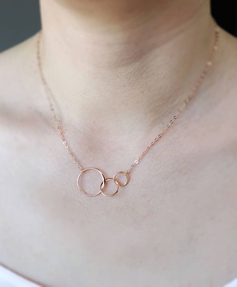 Peut inclure: Un collier en or rose avec trois cercles entrelac&eacute;s. Les cercles sont de tailles diff&eacute;rentes et sont reli&eacute;s &agrave; une cha&icirc;ne d&eacute;licate.