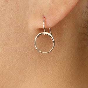May include: Silver hoop earrings with a simple, circular design. The earrings are small and delicate, and they hang from a small hook.