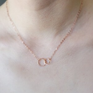 Pode incluir: Um delicado colar de ouro rosa com dois c&iacute;rculos entrela&ccedil;ados. A corrente &eacute; fina e delicada, e os c&iacute;rculos s&atilde;o pequenos e simples.