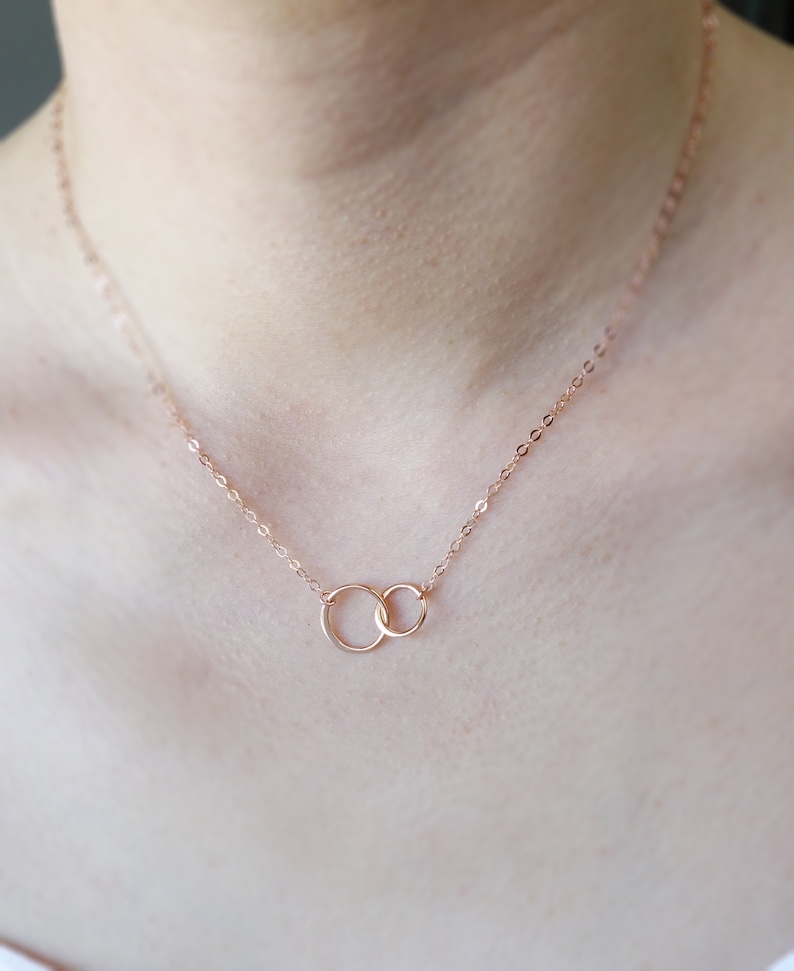 Pode incluir: Um delicado colar de ouro rosa com dois c&iacute;rculos entrela&ccedil;ados. A corrente &eacute; fina e delicada, e os c&iacute;rculos s&atilde;o pequenos e simples.