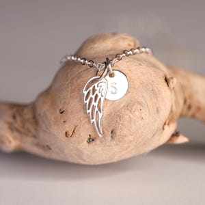 May include: A silver necklace with a delicate wing charm and a small round charm with the letter "S" engraved on it.