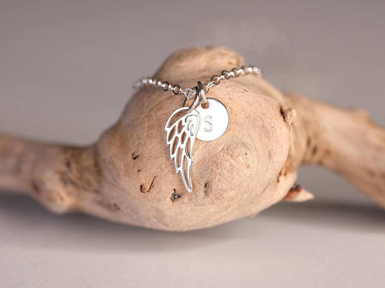 May include: A silver necklace with a delicate wing charm and a small round charm with the letter "S" engraved on it.