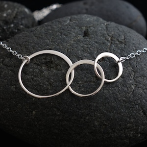 May include: Silver necklace with three interlocking circles, the circles are different sizes and are connected to a silver chain.