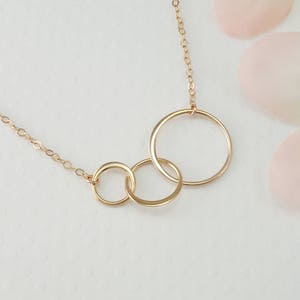 Peut inclure: Collier en or avec trois cercles entrelac&eacute;s. Les cercles sont de tailles diff&eacute;rentes et sont reli&eacute;s &agrave; une d&eacute;licate cha&icirc;ne en or.