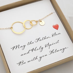 May include: Gold necklace with three interlocking circles and a charm with the letter C. The necklace is in a box with a white card that reads "May the Father, Son and Holy Spirit be with you always..."