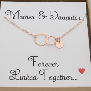 Pode incluir: Colar de ouro rosa com dois c&iacute;rculos entrela&ccedil;ados e um pequeno pingente com a letra 'B'. O colar &eacute; apresentado em uma caixa com o texto 'M&atilde;e e Filha Unidas para Sempre...' e um cora&ccedil;&atilde;o vermelho.