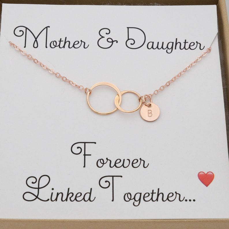 Pode incluir: Colar de ouro rosa com dois c&iacute;rculos entrela&ccedil;ados e um pequeno pingente com a letra 'B'. O colar &eacute; apresentado em uma caixa com o texto 'M&atilde;e e Filha Unidas para Sempre...' e um cora&ccedil;&atilde;o vermelho.