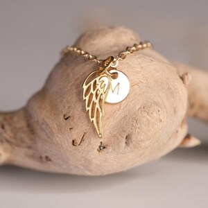 May include: Gold necklace with a delicate angel wing charm and a small round charm with the letter "M" engraved on it.