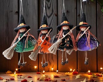 Op de afbeelding: Vier hangende Halloween heks poppen. Elke pop heeft een zwarte heksenhoed met een oranje gesp, rood haar en een bezem. De jurken zijn groen, oranje, zwart en paars. De poppen hangen aan een tak met decoratieve spinnen.