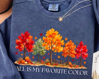 Puede incluir: Una sudadera azul marino de cuello redondo con un gráfico de árboles otoñales con hojas rojas, naranjas y amarillas. El texto "FALL IS MY FAVORITE COLOR" está impreso en blanco debajo de los árboles. Una pequeña calabaza se ve en la base.