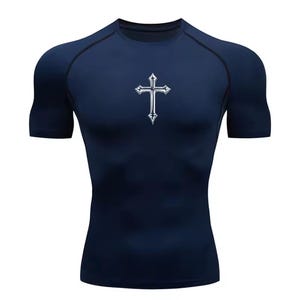 May include: Navy blue compression shirt with a silver cross design on the chest. The short-sleeved athletic top features a crew neck and black trim along the shoulders and sleeves. The shirt is made of a stretchy, form-fitting material.