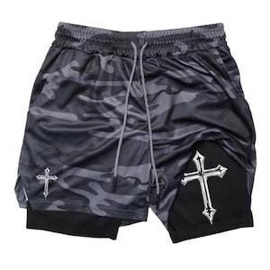 Puede incluir: Pantalones cortos deportivos de camuflaje en negro y gris con cintura con cordón. Los pantalones cortos presentan un diseño de cruz blanca en el lateral y una capa interior negra. Para actividades deportivas.