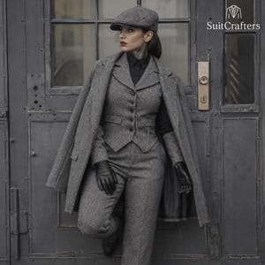 Op de afbeelding: Een driedelig grijs tweed pak bestaande uit een vest met knopen, een broek en een bijpassende overjas die over de schouders is gedrapeerd. De outfit bevat een platte pet, een zwart overhemd met kraag en zwarte leren handschoenen. De tekst SuitCrafters is zichtbaar.