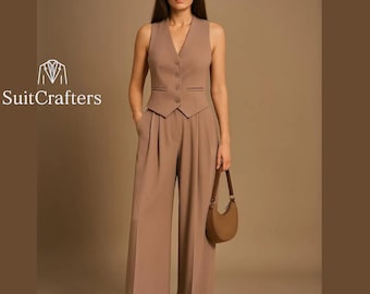 May include: A tan sleeveless vest with matching wide-leg trousers. The vest has a V-neck and button closure. A brown handbag is held in the hand. The logo "SuitCrafters" is visible on the left.