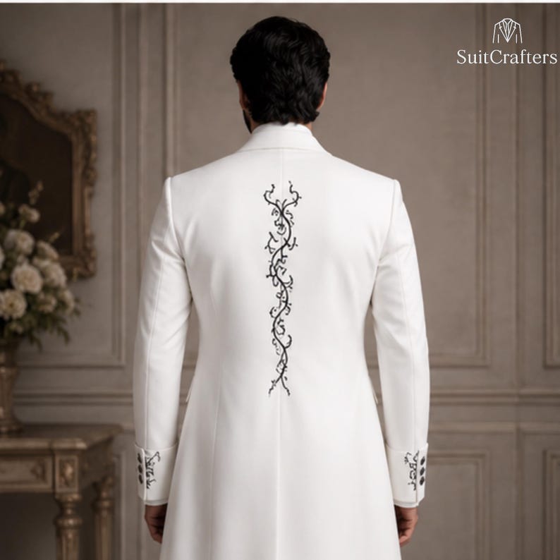 May include: A white long-length coat featuring a vertical black vine-like embroidery pattern running down the center of the back. The sleeves have matching black embroidery on the cuffs, each finished with a row of three small black buttons.
