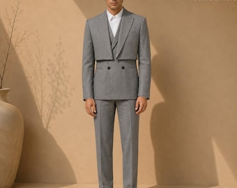 May include: A grey suit featuring a cropped double-breasted jacket with notched lapels and matching trousers. The ensemble is worn over a crisp white collared shirt and paired with white sneakers. The SuitCrafters logo is visible in the corner.