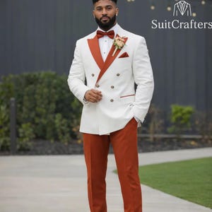 May include: A double-breasted white suit with rust-colored lapels and trousers. The suit features a rust-colored bow tie, pocket square, and trim. The image includes the text "SuitCrafters".