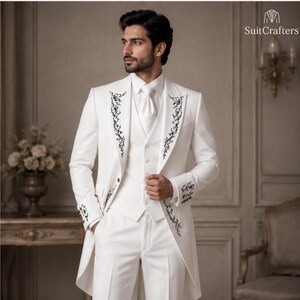 May include: A white tailcoat suit featuring a matching vest and trousers, adorned with intricate black floral embroidery along the lapels and cuffs. The ensemble includes a white necktie and is branded with the text SuitCrafters in the corner.