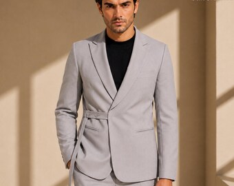 May include: A light gray blazer with a black shirt underneath. The blazer features a notched lapel, long sleeves, and a unique side-fastening strap detail with two buttons at the waist. The garment is tailored with a structured fit and clean lines.